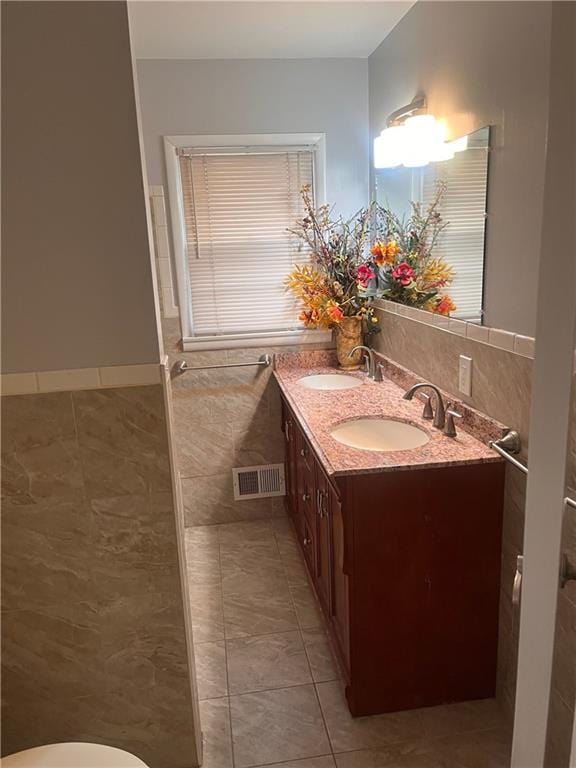 full bath with double vanity, visible vents, tile walls, and a sink