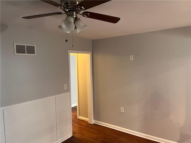 empty room featuring dark wood finished floors, a ceiling fan, visible vents, and baseboards