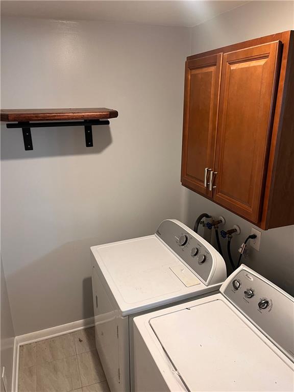 laundry room featuring separate washer and dryer, light tile patterned floors, cabinet space, and baseboards