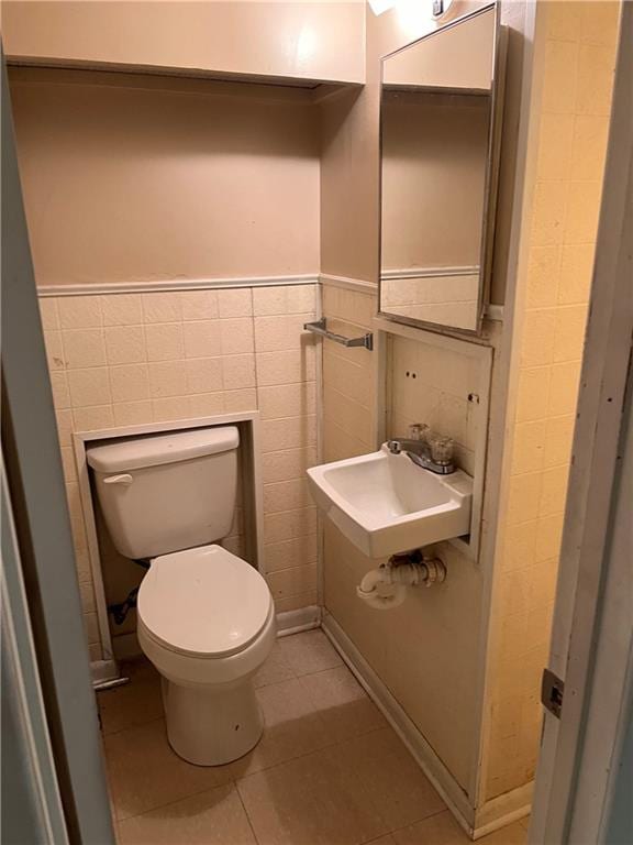 half bathroom with toilet, tile walls, wainscoting, and tile patterned flooring