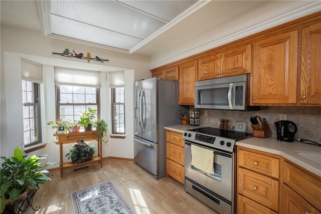 327 E Partridge Ave, Independence, MO 64055 - kitchen with brown cabinets, light wood-type flooring, light countertops, appliances with stainless steel finishes, and tasteful backsplash