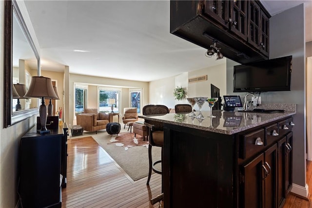 kitchen with wood finished floors, open floor plan, a breakfast bar area, a sink, and stone counters