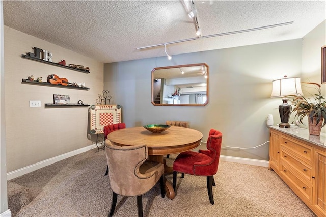 dining space featuring baseboards, light carpet, rail lighting, and a textured ceiling
