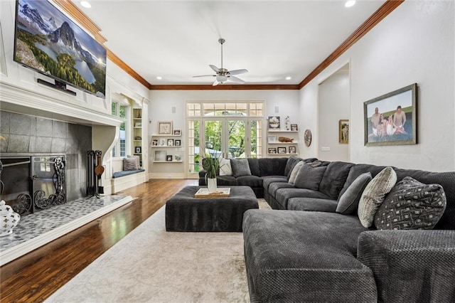 living room featuring ceiling fan, a tiled fireplace, recessed lighting, wood finished floors, and ornamental molding