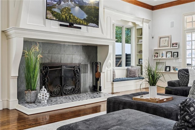 sitting room featuring a tiled fireplace, crown molding, wood finished floors, and built in shelves