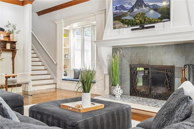 living room with stairway, a tiled fireplace, ornamental molding, and wood finished floors
