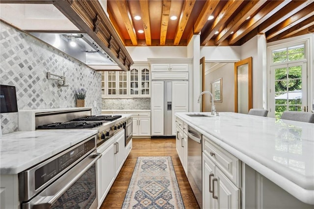 kitchen with exhaust hood, tasteful backsplash, wood finished floors, a sink, and built in appliances