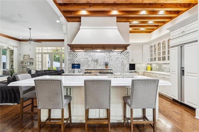 kitchen featuring backsplash, light countertops, glass insert cabinets, a breakfast bar, and custom range hood