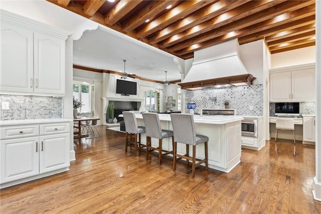 kitchen featuring white cabinets, a breakfast bar area, premium range hood, stainless steel microwave, and decorative backsplash