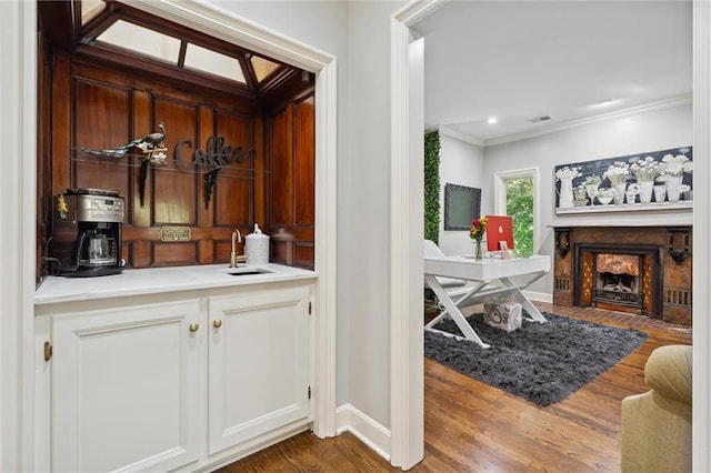 bar featuring crown molding, visible vents, a fireplace with flush hearth, wood finished floors, and a sink