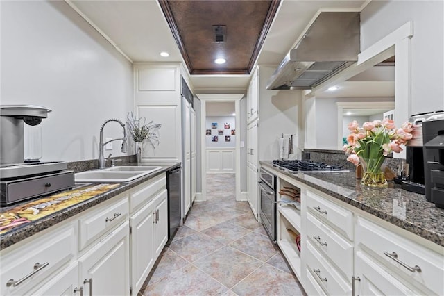 kitchen featuring stainless steel gas cooktop, dishwasher, a sink, white cabinetry, and wall chimney exhaust hood