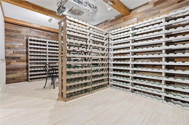 wine room with beamed ceiling, light wood finished floors, and wood walls