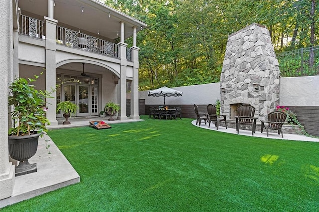 view of yard featuring a patio, an outdoor stone fireplace, french doors, and a balcony