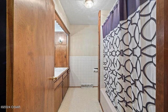 104 W Highland Ave, Nevada, MO 64772 - full bath with a textured ceiling, vanity, wainscoting, shower / tub combo with curtain, and tile walls