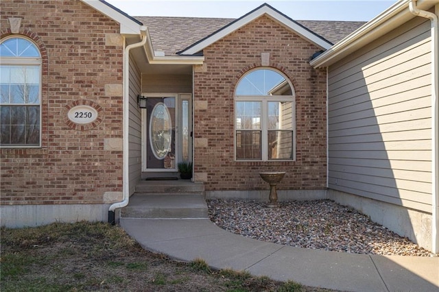 doorway to property featuring brick siding and roof with shingles