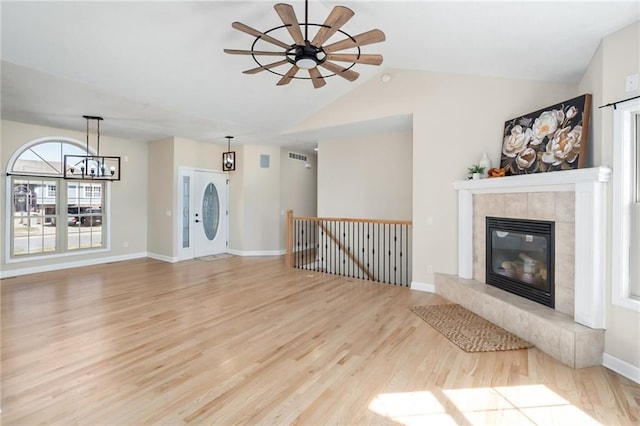 unfurnished living room with baseboards, lofted ceiling, ceiling fan with notable chandelier, a fireplace, and wood finished floors