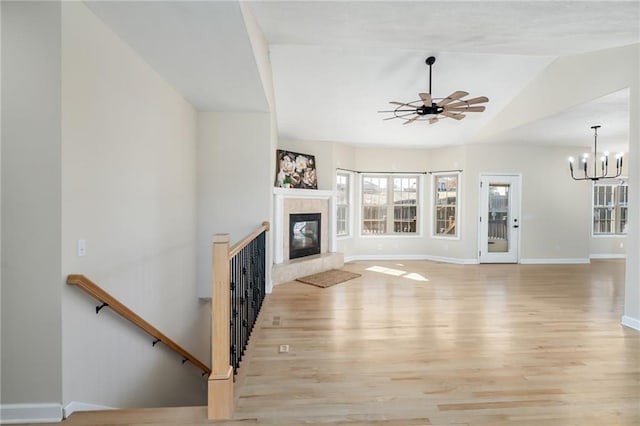 unfurnished living room featuring baseboards, lofted ceiling, ceiling fan with notable chandelier, light wood-style floors, and a glass covered fireplace