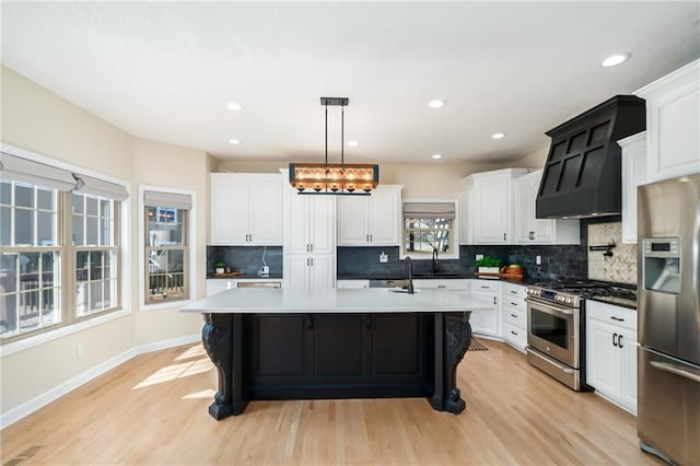 kitchen featuring a center island with sink, premium range hood, light wood-style flooring, stainless steel appliances, and white cabinetry