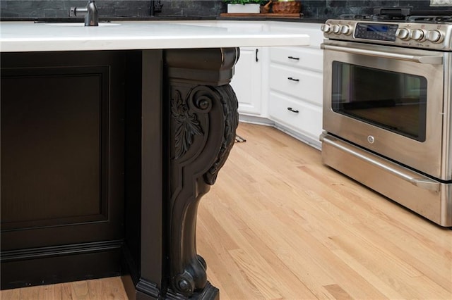 kitchen featuring tasteful backsplash, light wood-style flooring, stainless steel gas range, and white cabinetry