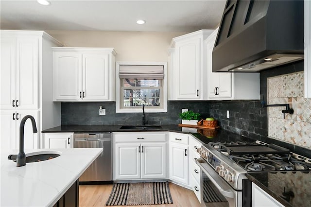 kitchen featuring a sink, wall chimney range hood, white cabinetry, and stainless steel appliances