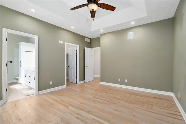 unfurnished bedroom with light wood finished floors, recessed lighting, a raised ceiling, and baseboards