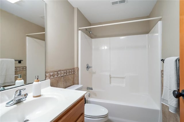 bathroom with visible vents, tile walls, toilet, vanity, and  shower combination