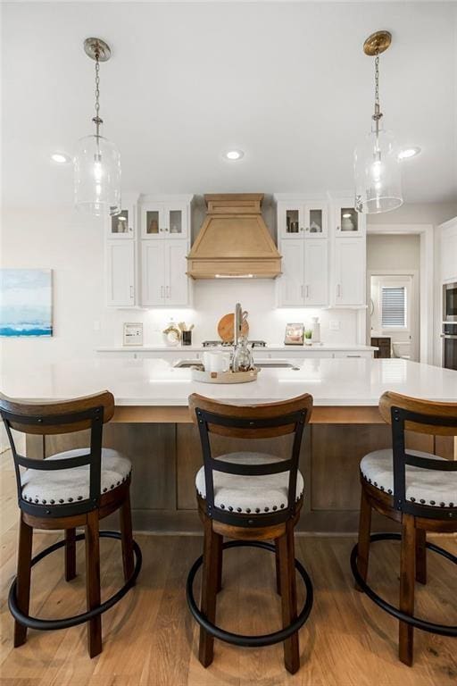 13021 W 174th Pl, Overland Park, KS 66221 - kitchen with custom exhaust hood, light countertops, stainless steel appliances, white cabinetry, and wood finished floors