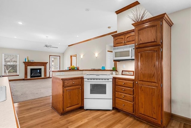 kitchen with light countertops, a tile fireplace, a peninsula, and white appliances