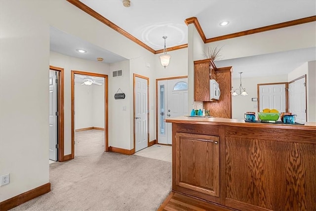 kitchen with ornamental molding, visible vents, light carpet, white microwave, and brown cabinets