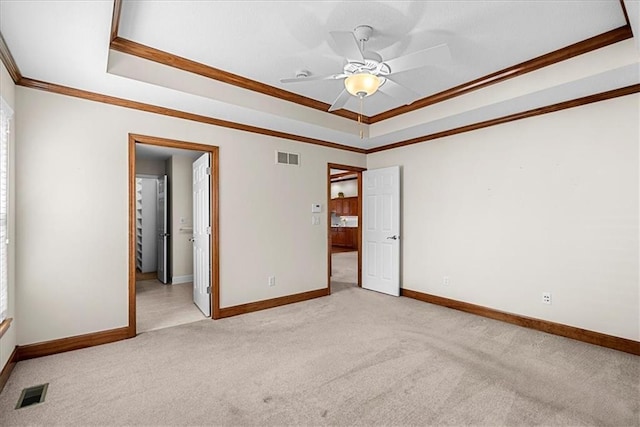 carpeted spare room with a tray ceiling, baseboards, visible vents, and ornamental molding