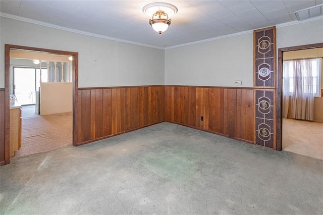 carpeted empty room featuring ornamental molding, visible vents, wainscoting, and wood walls