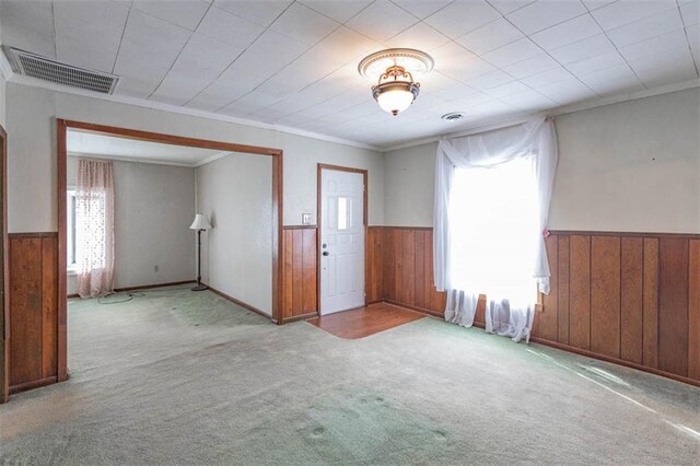 carpeted empty room with visible vents, wood walls, and wainscoting