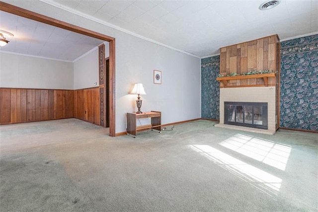 unfurnished living room featuring crown molding, a brick fireplace, wainscoting, visible vents, and carpet