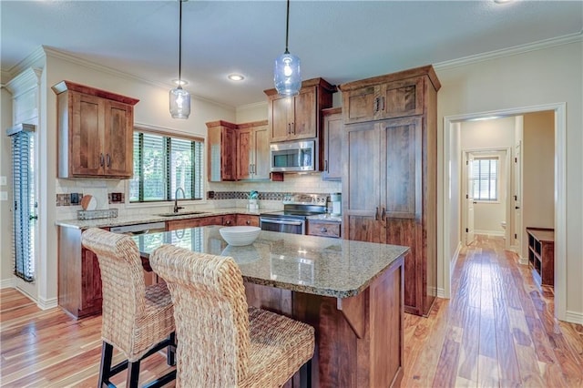 kitchen with appliances with stainless steel finishes, a sink, light wood-style floors, tasteful backsplash, and hanging light fixtures