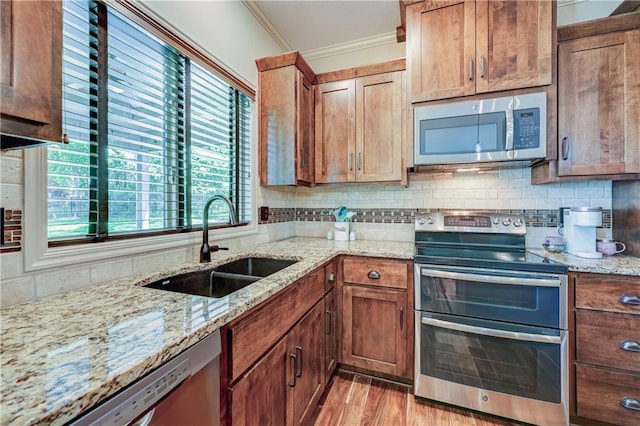 kitchen featuring stainless steel appliances, a sink, ornamental molding, plenty of natural light, and backsplash