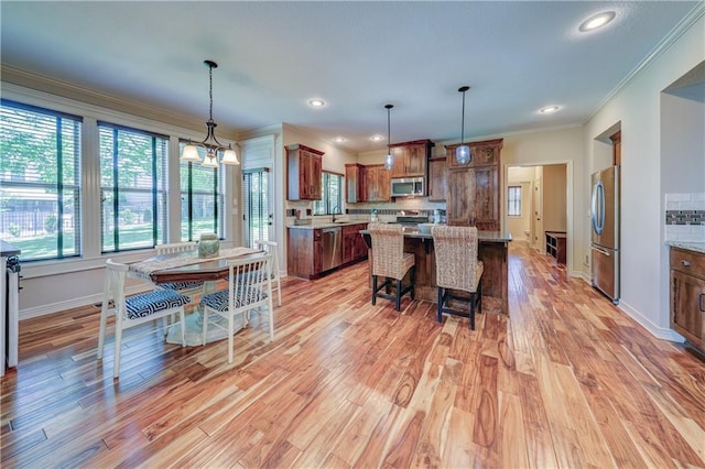 kitchen with appliances with stainless steel finishes, crown molding, light wood finished floors, a center island, and a breakfast bar