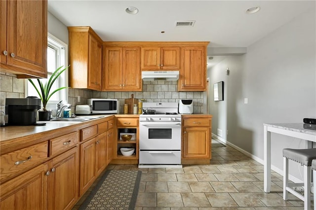 kitchen featuring white gas stove, tasteful backsplash, stainless steel microwave, under cabinet range hood, and visible vents