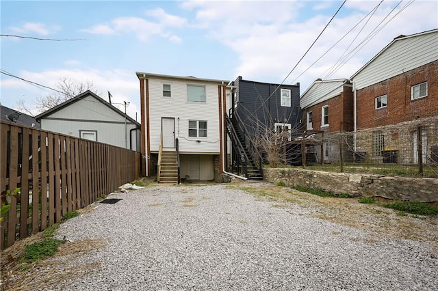 back of house with a fenced backyard, stairs, and gravel driveway