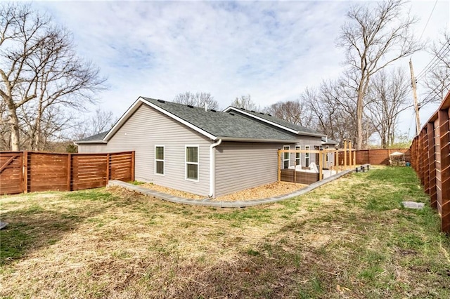 back of property with a lawn, a shingled roof, and a fenced backyard