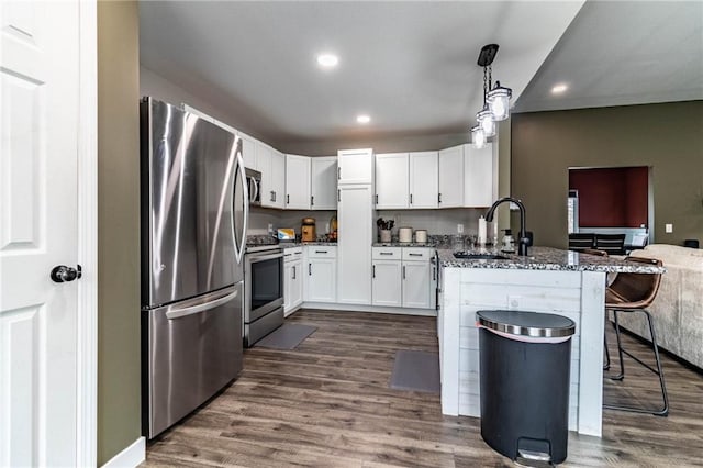 kitchen featuring a peninsula, stainless steel appliances, dark wood-type flooring, a sink, and a breakfast bar area