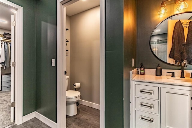 full bathroom featuring toilet, vanity, wood finished floors, a walk in closet, and baseboards