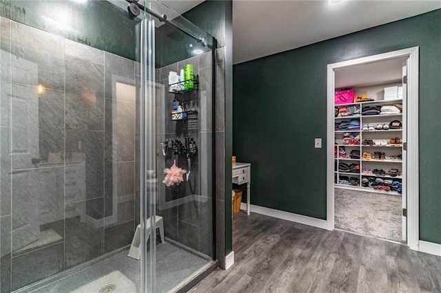 bathroom featuring baseboards, wood finished floors, a stall shower, and a walk in closet