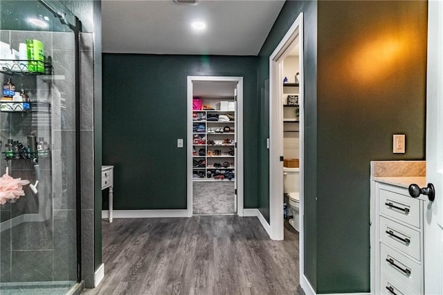 bathroom with toilet, a shower stall, wood finished floors, a spacious closet, and baseboards