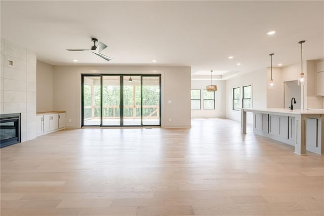 907 Reed Dr, Raymore, MO 64083 - unfurnished living room featuring light wood-style flooring, recessed lighting, a tiled fireplace, and a ceiling fan