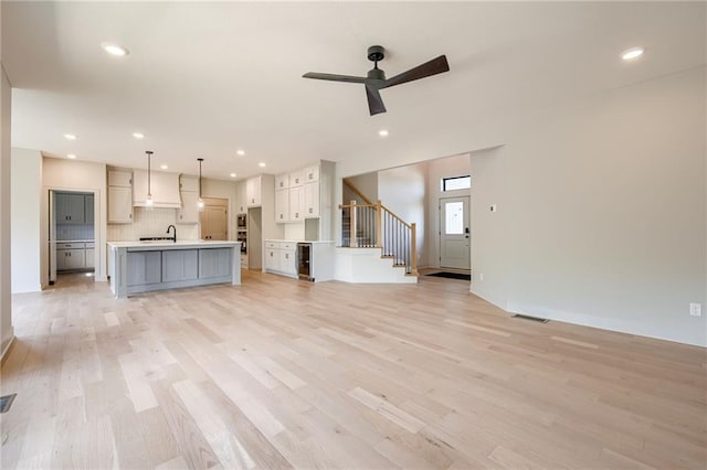907 Reed Dr, Raymore, MO 64083 - unfurnished living room featuring light wood-type flooring, ceiling fan, stairway, and recessed lighting