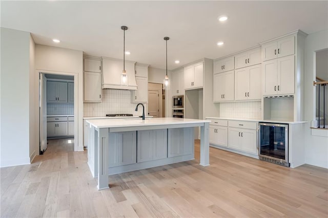 907 Reed Dr, Raymore, MO 64083 - kitchen with wine cooler, tasteful backsplash, appliances with stainless steel finishes, light wood-style floors, and light countertops