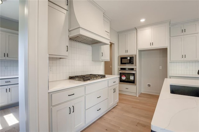 907 Reed Dr, Raymore, MO 64083 - kitchen featuring stainless steel appliances, custom exhaust hood, tasteful backsplash, light stone countertops, and light wood-style flooring