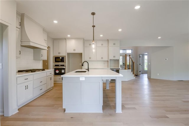907 Reed Dr, Raymore, MO 64083 - kitchen featuring black microwave, gas cooktop, light wood-style floors, oven, and an island with sink