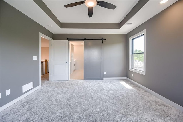 907 Reed Dr, Raymore, MO 64083 - unfurnished bedroom with a raised ceiling, carpet flooring, a barn door, and a ceiling fan