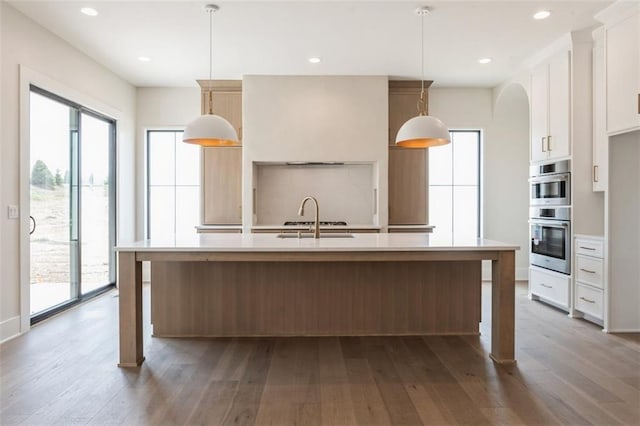17041 Earnshaw St, Overland Park, KS 66221 - kitchen with stainless steel double oven, light countertops, wood-type flooring, white cabinets, and a kitchen island with sink